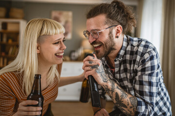 Adult couple sing karaoke on microphone and hold bottle of beer at home