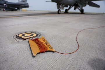 Electrical grounding cables are seen on a runway. Military fighter aircraft in the background. - 787554490