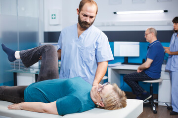 Physiotherapist helping aged woman with leg muscle pain in osteopathy clinic. Chiropractor...