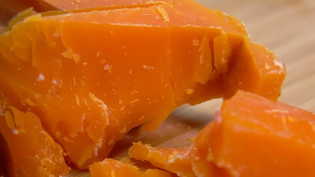 A knife breaks off a piece of hard Mimolette cheese close-up. High quality 4k footage