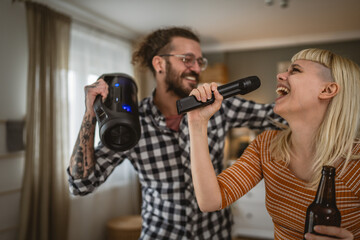 Adult couple sing karaoke on microphone and hold bottle of beer at home