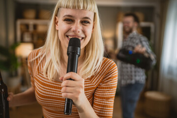 Adult woman sing karaoke on microphone with man in the background