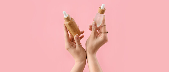 Hands holding cosmetic products on pink background