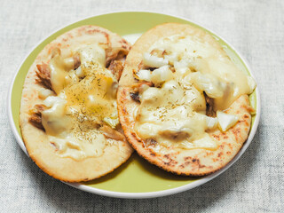 Meal with two pita bread with chopped cooked chicken fillet and melted cheese on a green plate and light color table clothes. Pizza style dish. Quick lunch.