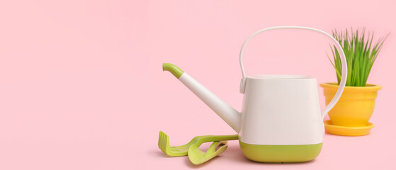 Watering can with gardening tools and grass on pink background