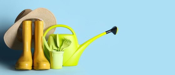 Composition with watering can, rubber boots and hat on blue background. Garden tools