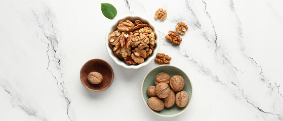 Bowls of tasty walnuts on white marble background