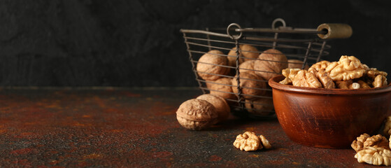 Bowl and basket of tasty walnuts on table against black wall