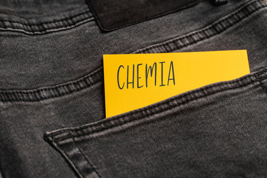 Yellow card with a handwritten inscription "Chemia", inserted into the pocket of gray pants jeasnow (selective focus), translation: chemistry