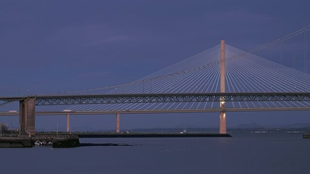 Static clip of two bridges and cars moving across them. 4k video of a large bridge in the evening. Forth Bridge and Queensferry Crossing Bridge, Scotland, United Kingdom