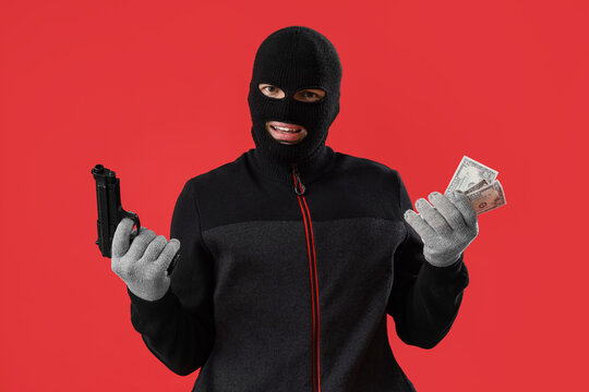 Male burglar with gun and money on red background