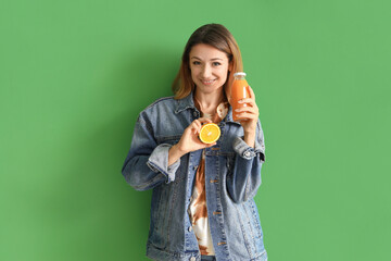 Young woman with bottle of juice and orange on green background