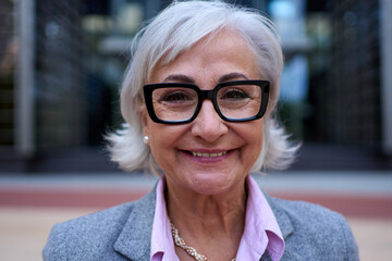 Portrait of mature Caucasian business woman with glasses and gray hair in formal suit smiling...
