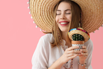 Young woman in sombrero hat with cactus on pink background, closeup. Mexico's Day of the Dead (El...