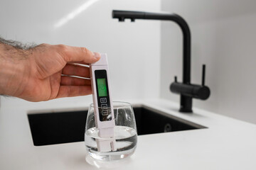Man hand immerses TDS tester or conductometer into the water in glass. demonstrates that the water...