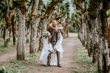 Valmiera, Latvia- July 28, 2024 - A groom giving a piggyback ride to his bride in a white wedding...