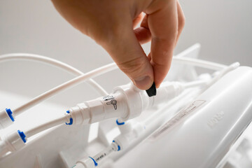 Man hand connect tubes in osmosis water purification filter for home use.