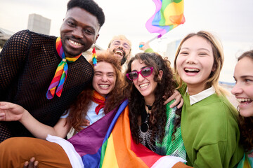 A happy crowd of LGBT people wearing colorful smiling for a picture with a rainbow flag at a fun...