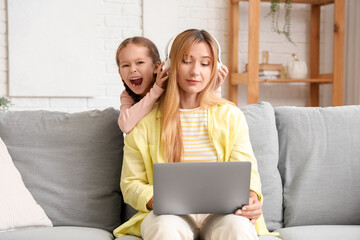 Working young woman in headphones stressed of her noisy little daughter at home
