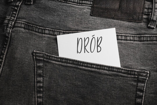 White card with a handwritten inscription "dr&oacute;b", inserted into the pocket of gray pants jeasnow (selective focus), translation: roads