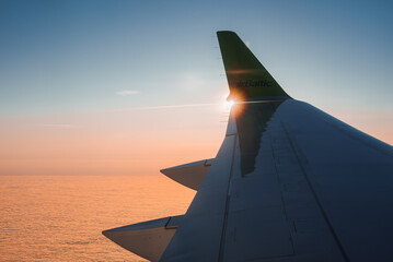 Wing of modern Airbaltic aircraft flying in cloudy sunset sky during a trip