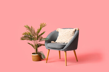 Modern grey armchair with pillow and flowerpot on pink background