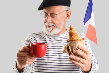 Senior man with flag of France, coffee cup and croissant on light background, closeup