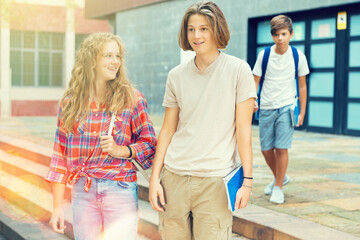 Two teenagers boy and girl walking home after finishing college lessons on autumn day