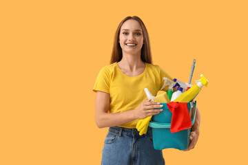 Pretty young woman with cleaning supplies on yellow background