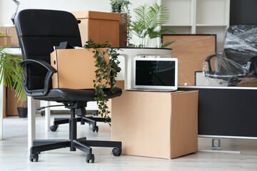 Interior of modern office with chair, laptop and cardboard boxes on moving day