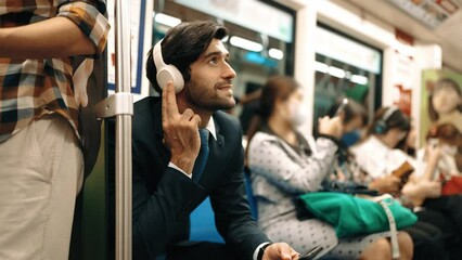 Smiling handsome male investor listening relaxing music while sitting on train. Professional business man enjoy listening music while using public transport to workplace. Blurred background. Exultant.