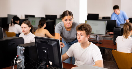 Young woman teacher helping concentrated teen male student with his work in college computer class