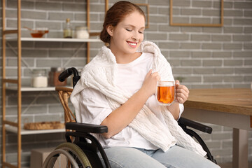 Young redhead woman in wheelchair with cup of tea at home