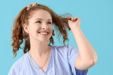Young redhead woman with ponytail and scrunchy on blue background, closeup