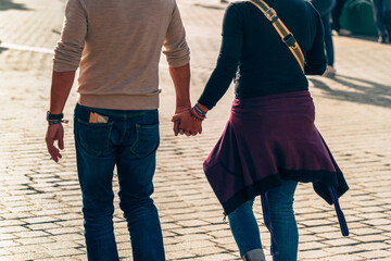 Love and urban lifestyle are captured as the couple walks hand in hand in the backlit sunlight,...