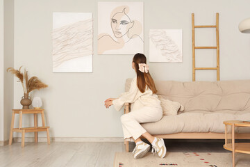 Young woman on sofa looking at stylish paintings in living room