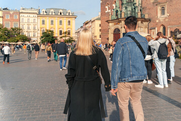 A Gen Z couple strolls through a vibrant city square surrounded by historic architecture under a...