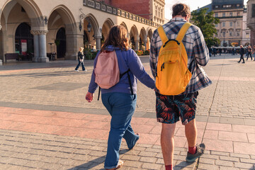 A couple of tourists with backpacks walk through the busy town square of the old town on a sunny...