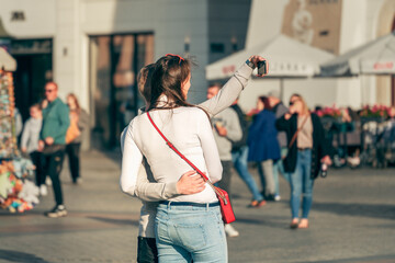 A Gen Z couple takes a smartphone selfie against a vibrant cityscape, embodying the essence of city...