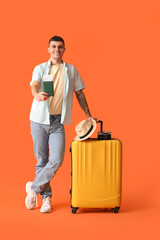 Young male tourist with suitcase and passport on orange background