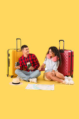 Couple of tourists with suitcases, passports and map sitting on yellow background