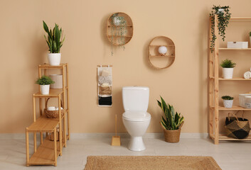 Interior of stylish bathroom with houseplants and ceramic toilet bowl near beige wall