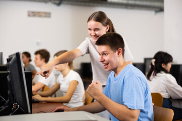 Positive young boy and girl using personal computer together, enjoying computer game.