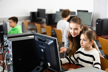 Teacher helping young girl to solve computer problem during lesson.
