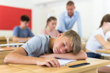 Tired bored teenage schoolboy sleeping at desk closeup - Powered by Adobe
