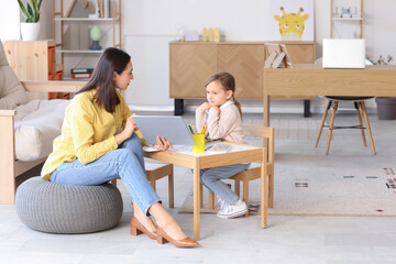 Female psychologist working with little girl at table in office