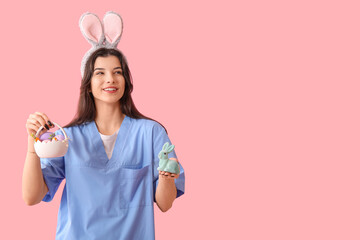 Female doctor in bunny ears with Easter rabbit and eggs on pink background