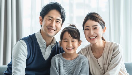 Obraz premium A young Japanese couple and their daughter, all smiling at the camera. Loving mother and father with kids enjoying time together at home sofa