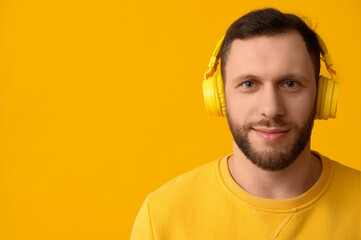 Young man in modern headphones on yellow background