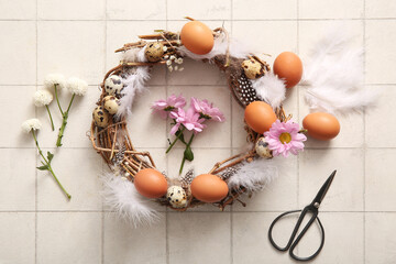 Supplies for creating Easter wreath with eggs, flowers and feathers on white tile background